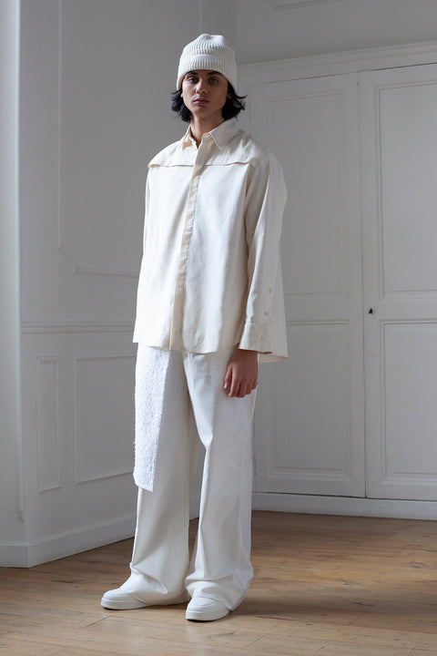 Medhi is wearing White Canvas sustainable natural beige color, organic cotton oversized, genderless, inclusive, seasonless casual shirt, size S/M styled with white cotton trousers. The Essential shirt has minimal modern aesthetics design allowing comfort and bringing self-confidence. A limited-edition production is made locally in France to reduce environmental impact and guarantee high quality and durability of the products.