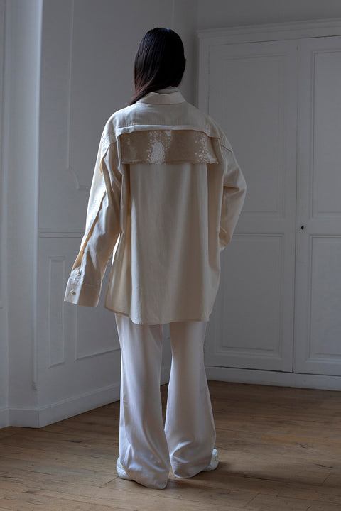 SiJia is wearing White Canvas sustainable natural beige color, organic cotton oversized, genderless, inclusive, seasonless casual shirt, size S/M styled with wool trousers. The Essential shirt has minimal modern aesthetics design allowing comfort and bringing self-confidence. A limited-edition production is made locally in France to reduce environmental impact and guarantee high quality and durability of the products.