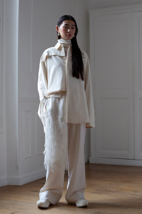 SiJia is wearing White Canvas sustainable natural beige color, organic cotton oversized, genderless, inclusive, seasonless casual shirt, size S/M styled with wool trousers. The Essential shirt has minimal modern aesthetics design allowing comfort and bringing self-confidence. A limited-edition production is made locally in France to reduce environmental impact and guarantee high quality and durability of the products.