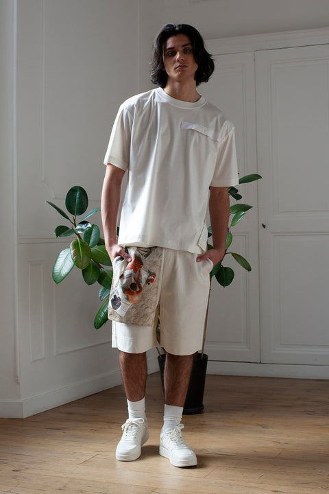 Medhi is wearing the White Canvas denim shorts styled with the Newspaper vertical panel made from deadstock cotton poplin. The panel has an exclusive print of a photo by the photographer Henrique Soares. Attach the panel to the essential pieces to personalize them and wear them your unique way. It is the perfect creative summer accessory.