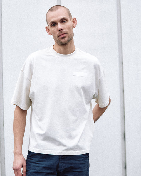 A male model is wearing the White Canvas Originals sustainable, oversized, genderless t-shirt, one size. The organic cotton natural color t-shirt has minimal modern aesthetics design allowing comfort and bringing self-confidence. This limited edition collection is made in Portugal to reduce environmental impact and guarantee high quality and durability of the products. There is a photo by the photographer Henrique Soares at the back of the t-shirt.