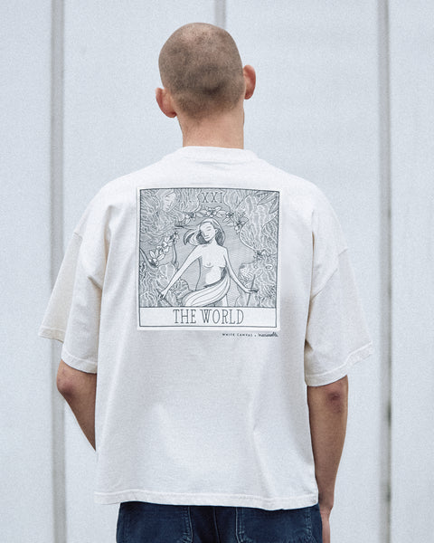 A male model is wearing the White Canvas Originals sustainable, oversized, genderless t-shirt, one size. The organic cotton natural color t-shirt has minimal modern aesthetics design allowing comfort and bringing self-confidence. This limited edition collection is made in Portugal to reduce environmental impact and guarantee high quality and durability of the products. There is an illustration of a tarot card by the artist Maria Robla at the back of the t-shirt.