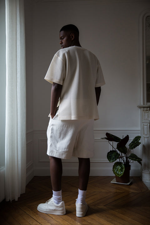 Thierno is wearing White Canvas sustainable mesh oversized, genderless, seasonless t-shirt, one size. The mesh t-shirt has minimal modern aesthetics design allowing comfort and bringing self-confidence. This unique piece is made locally in Paris to reduce environmental impact and guarantee high quality and durability of the products.
