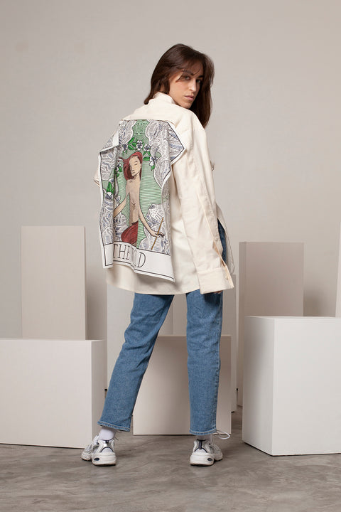 Léa is wearing the White Canvas ESSENTIAL SHIRT styled with THE WORLD foulard and square panel made from leftover deadstock silk fabric. The foulard has an exclusive design inspired by tarot cards drawn by the artist Maria Robla, printed with black artisanal eco-friendly ink locally in Paris and hand painted by the artist. Wear the foulard alone or attach it to the essential pieces to personalize them and wear them your unique way. Your perfect summer accessory. White Canvas x Maria Robla.