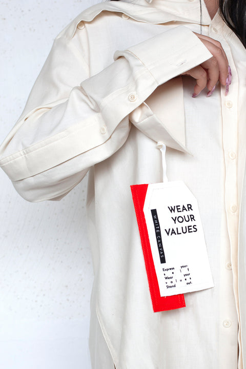 The White Canvas ESSENTIAL SHIRT with a limited edition tag made in white and red cotton poplin leftover deadstock fabrics and with black artisanal eco-friendly screen print done locally in Paris in collaboration with RoStudio. Attach the panel to the essential pieces to personalize them and wear them your unique way. The tag is sold with key holder in recycled plastic made in collaboration with Samji Atelier
