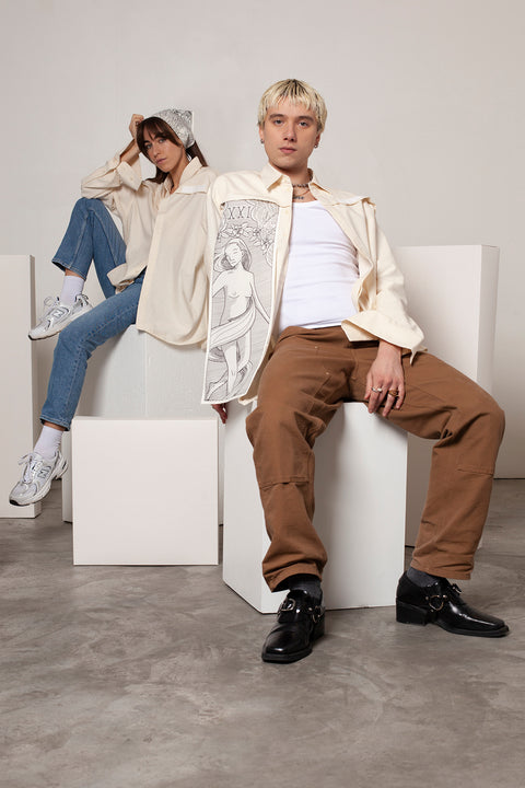 Léa and Clément are wearing the White Canvas ESSENTIAL SHIRT styled with THE WORLD triangular panel & bandana made from leftover deadstock white cotton poplin. The bandana has an exclusive design inspired by tarot cards drawn by the artist Maria Robla and printed with black artisanal eco-friendly ink locally in Paris in collaboration with RoStudio. Wear the black and white bandana alone or attach it to the essential pieces to personalize them and wear them your unique way. Your perfect summer accessory.
