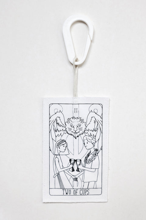 THE TWO OF CUPS tag is made from leftover deadstock white cotton poplin. The black and white tag has an exclusive design inspired by tarot cards drawn by the artist Maria Robla and is printed in collaboration with RoStudio. Wear the tag alone or attach it to the essential pieces to personalize them. The tag is sold with key holder in recycled plastic made in collaboration with Samji Atelier. White Canvas x Maria Robla.