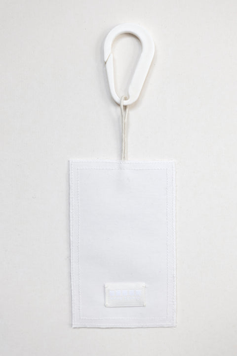 THE TWO OF CUPS tag is made from leftover deadstock white cotton poplin. The black and white tag has an exclusive design inspired by tarot cards drawn by the artist Maria Robla and is printed in collaboration with RoStudio. Wear the tag alone or attach it to the essential pieces to personalize them. The tag is sold with key holder in recycled plastic made in collaboration with Samji Atelier. White Canvas x Maria Robla.