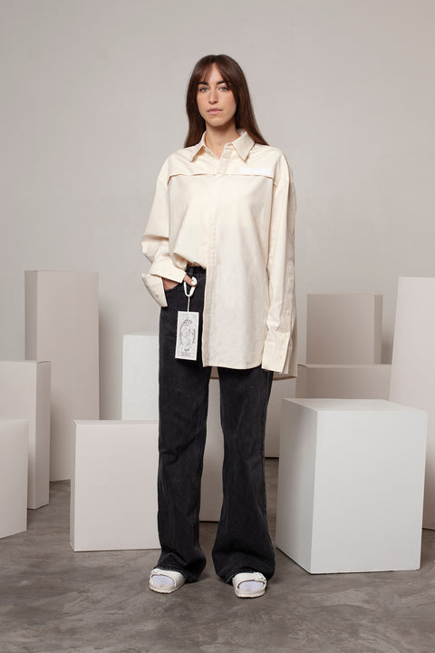 Léa is wearing the White Canvas ESSENTIAL SHRT styled with THE WORLD tag made from leftover deadstock white cotton poplin. The black and white tag has an exclusive design inspired by tarot cards drawn by the artist Maria Robla and is printed in collaboration with RoStudio. Wear the tag alone or attach it to the essential pieces to personalize them. The tag is sold with key holder in recycled plastic made in collaboration with Samji Atelier. White Canvas x Maria Robla.