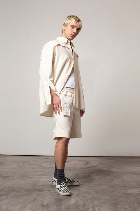 Clément is wearing the White Canvas ESSENTIAL SHORT styled with THE WORLD tag made from leftover deadstock white cotton poplin. The black and white tag has an exclusive design inspired by tarot cards drawn by the artist Maria Robla and is printed in collaboration with RoStudio. Wear the tag alone or attach it to the essential pieces to personalize them. The tag is sold with key holder in recycled plastic made in collaboration with Samji Atelier. White Canvas x Maria Robla.
