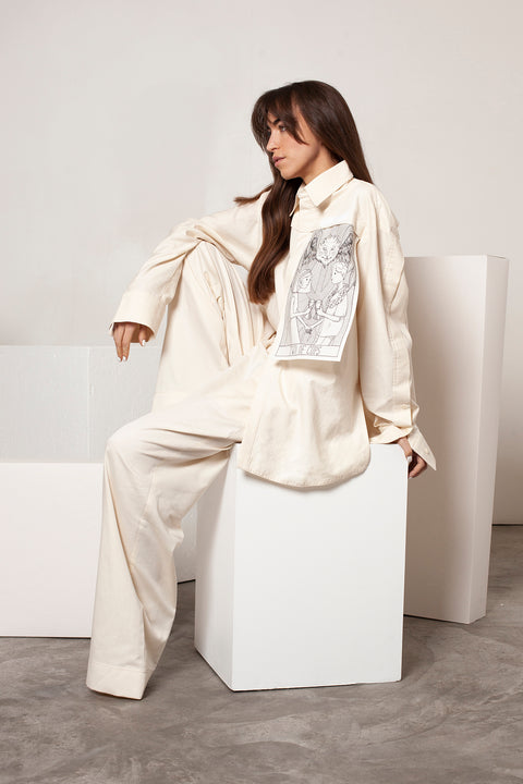 Léa is wearing the White Canvas ESSENTIAL SHIRT styled with THE TWO OF CUPS vertical panel made from leftover deadstock white cotton poplin. The panel has an exclusive design inspired by tarot cards drawn by the artist Maria Robla and printed with black artisanal eco-friendly ink locally in Paris in collaboration with RoStudio. Attach the black and white panel to the essential pieces to personalize them and wear them your unique way. Your perfect summer accessory.