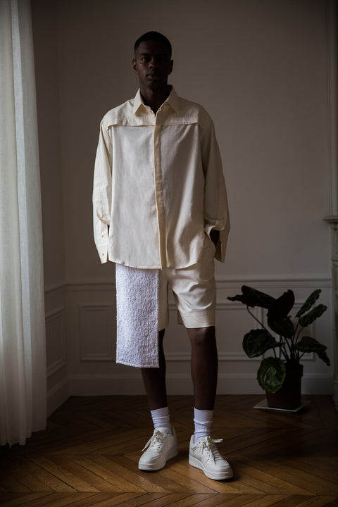Thierno is wearing White Canvas sustainable natural beige color, organic cotton, genderless, inclusive, casual short, size M styled with a white tank top. The Essential short has minimal modern aesthetics design allowing comfort and bringing self-confidence. A limited-edition production is made locally in France to reduce environmental impact and guarantee high quality and durability of the products. 
