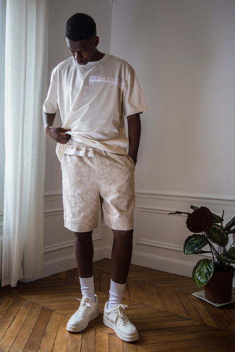 Thierno is wearing White Canvas sustainable cotton jacquard genderless casual shorts, size S. The jacquard shorts have minimal modern aesthetics design allowing comfort and bringing self-confidence. This unique piece is made locally in Paris to reduce environmental impact and guarantee high quality and durability of the products.