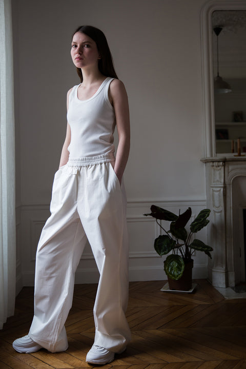 Dalva is wearing White Canvas sustainable cotton stripes genderless, seasonless casual checks trousers, size M. The white cotton stripes trousers have minimal modern aesthetics design allowing comfort and bringing self-confidence. This unique piece is made locally in Paris to reduce environmental impact and guarantee high quality and durability of the products.