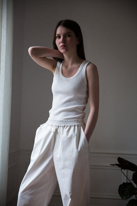 Dalva is wearing White Canvas sustainable cotton stripes genderless, seasonless casual checks trousers, size M. The white cotton stripes trousers have minimal modern aesthetics design allowing comfort and bringing self-confidence. This unique piece is made locally in Paris to reduce environmental impact and guarantee high quality and durability of the products.