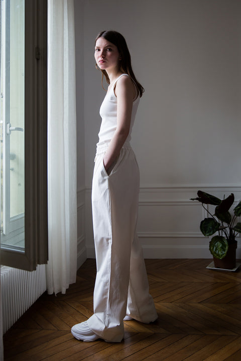 Dalva is wearing White Canvas sustainable cotton stripes genderless, seasonless casual checks trousers, size M. The white cotton stripes trousers have minimal modern aesthetics design allowing comfort and bringing self-confidence. This unique piece is made locally in Paris to reduce environmental impact and guarantee high quality and durability of the products.