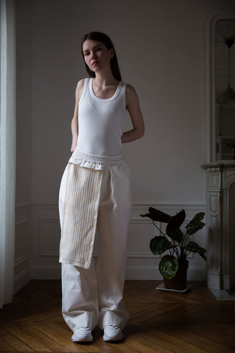 Dalva is wearing White Canvas sustainable cotton stripes genderless, seasonless casual checks trousers, size M. The white cotton stripes trousers have minimal modern aesthetics design allowing comfort and bringing self-confidence. This unique piece is made locally in Paris to reduce environmental impact and guarantee high quality and durability of the products.