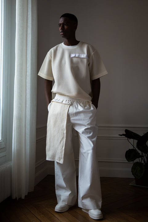 Thierno is wearing White Canvas sustainable cotton stripes genderless, seasonless casual checks trousers, size L. The white cotton stripes trousers have minimal modern aesthetics design allowing comfort and bringing self-confidence. This unique piece is made locally in Paris to reduce environmental impact and guarantee high quality and durability of the products.