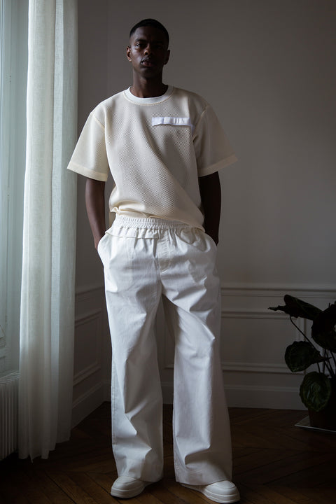 Thierno is wearing White Canvas sustainable cotton stripes genderless, seasonless casual checks trousers, size L. The white cotton textured trousers have minimal modern aesthetics design allowing comfort and bringing self-confidence. This unique piece is made locally in Paris to reduce environmental impact and guarantee high quality and durability of the products.