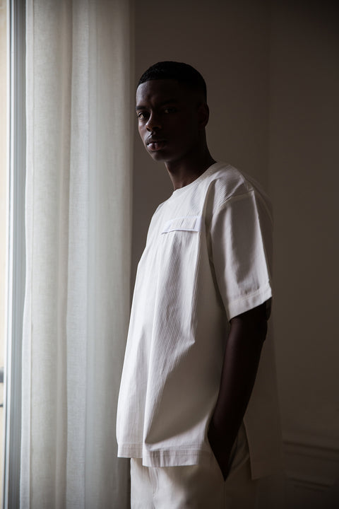 Thierno is wearing White Canvas sustainable white, oversized, genderless, seasonless t-shirt, one size. The cotton stripes t-shirt has minimal modern aesthetics design allowing comfort and bringing self-confidence. This unique piece is made locally in Paris to reduce environmental impact and guarantee high quality and durability of the products. 