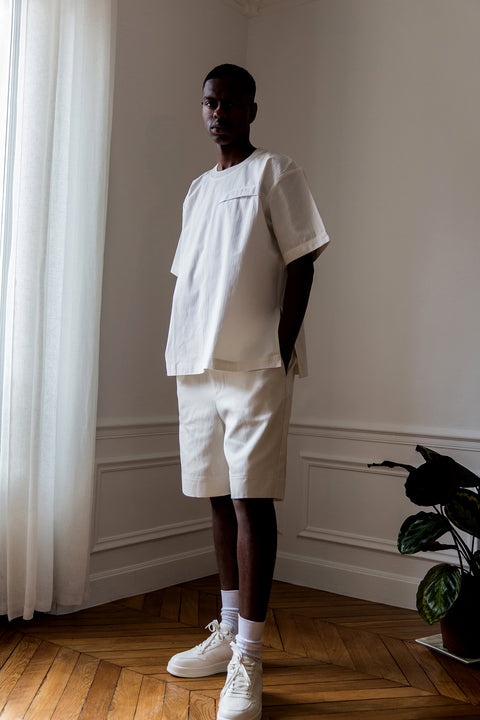 Thierno is wearing White Canvas sustainable white, oversized, genderless, seasonless t-shirt, one size. The cotton stripes t-shirt has minimal modern aesthetics design allowing comfort and bringing self-confidence. This unique piece is made locally in Paris to reduce environmental impact and guarantee high quality and durability of the products. 
