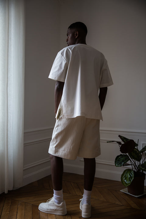 Thierno is wearing White Canvas sustainable white, oversized, genderless, seasonless t-shirt, one size. The cotton stripes t-shirt has minimal modern aesthetics design allowing comfort and bringing self-confidence. This unique piece is made locally in Paris to reduce environmental impact and guarantee high quality and durability of the products. 