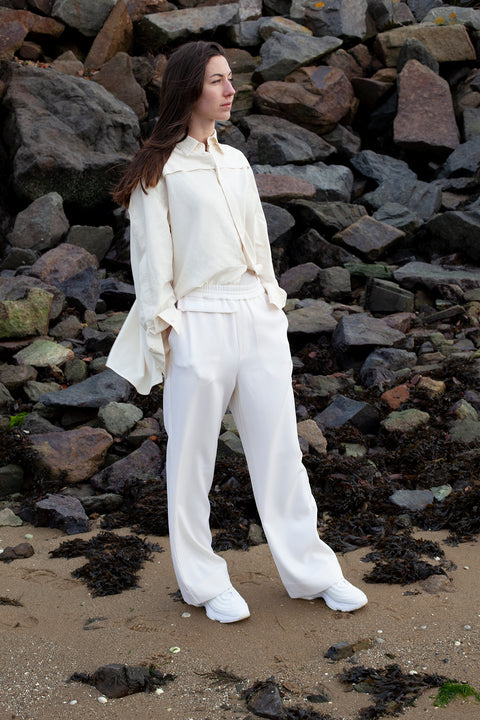 Romane is wearing White Canvas wool natural color, genderless, seasonless casual trousers, size S. The Essential wool trousers have minimal modern aesthetics design allowing comfort and bringing self-confidence. This unique piece is made locally in Paris to reduce environmental impact and guarantee high quality and durability of the products. 