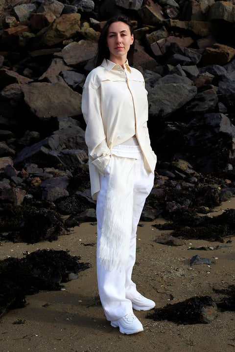 Romane is wearing the White Canvas ESSENTIAL SHIER AND TROUSERS styled with the silver fringes vertical fabric panel made from leftover deadstock fabrics. The silver fringes panel is an exclusive unique sustainable piece made in France. It is made to be attached to the essential pieces to personalize them and wear them your unique way.