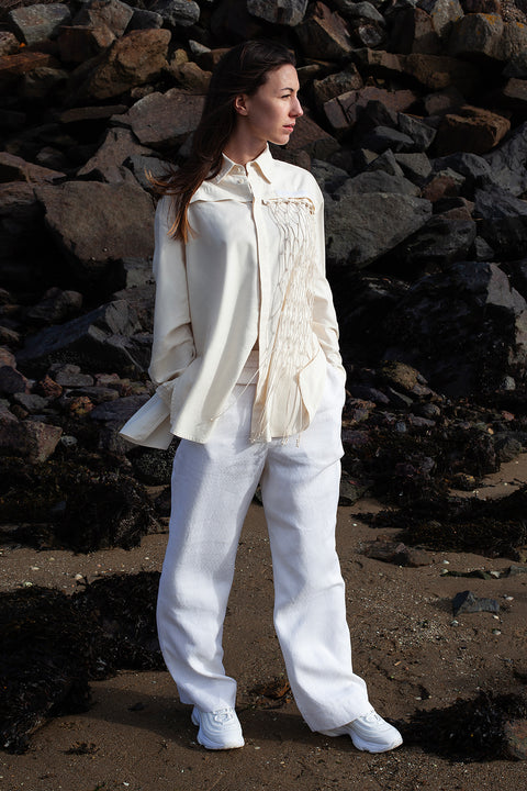 Romane is wearing the White Canvas ESSENTIAL SHIRT AND TROUSERS styled with the net vertical panel with recycled beads made from leftover deadstock fabrics. The net vertical panel with recycled beads is an exclusive unique sustainable piece made in France. It is made to be attached to the essential pieces to personalize them and wear them your unique way.