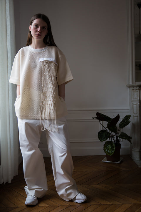 Dalva is wearing the White Canvas net t-shirt and white cotton trousers styled with the net vertical panel with recycled beads made from leftover deadstock fabrics. The net vertical panel with recycled beads is an exclusive unique sustainable piece made in France. It is made to be attached to the essential pieces to personalize them and wear them your unique way.