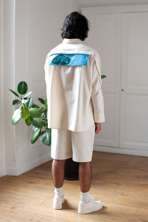 Medhi is wearing the White Canvas ESSENTIAL SHIRT styled with the glass horizontal panel made from deadstock white cotton poplin. The panel has an exclusive print of a photo by the photographer Henrique Soares. Attach the panel to the essential pieces to personalize them and wear them your unique way. It is the perfect creative summer accessory.