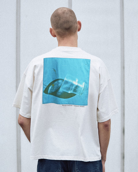 A male model is wearing the White Canvas Originals sustainable, oversized, genderless t-shirt, one size. The organic cotton natural color t-shirt has minimal modern aesthetics design allowing comfort and bringing self-confidence. This limited edition collection is made in Portugal to reduce environmental impact and guarantee high quality and durability of the products. There is a photo by the photographer Henrique Soares at the back of the t-shirt.