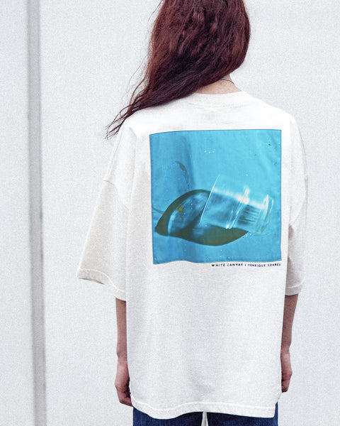 A female model is wearing the White Canvas Originals sustainable, oversized, genderless t-shirt, one size. The organic cotton natural color t-shirt has minimal modern aesthetics design allowing comfort and bringing self-confidence. This limited edition collection is made in Portugal to reduce environmental impact and guarantee high quality and durability of the products. There is a photo by the photographer Henrique Soares at the back of the t-shirt.