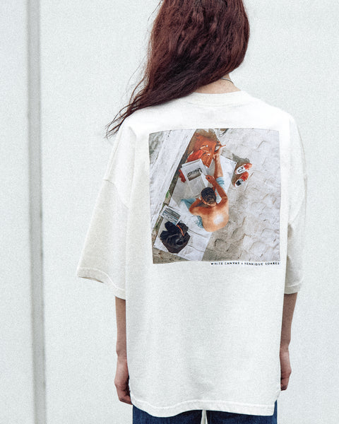 A female model is wearing the White Canvas Originals sustainable, oversized, genderless t-shirt, one size. The organic cotton natural color t-shirt has minimal modern aesthetics design allowing comfort and bringing self-confidence. This limited edition collection is made in Portugal to reduce environmental impact and guarantee high quality and durability of the products. There is a photo by the photographer Henrique Soares at the back of the t-shirt.