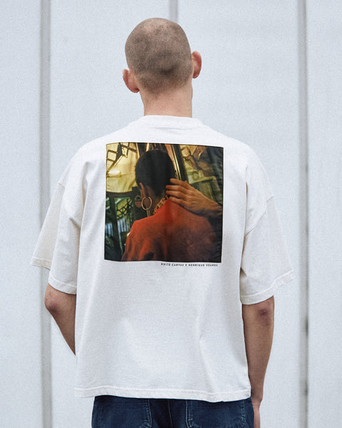 A male model is wearing the White Canvas Originals sustainable, oversized, genderless t-shirt, one size. The organic cotton natural color t-shirt has minimal modern aesthetics design allowing comfort and bringing self-confidence. This limited edition collection is made in Portugal to reduce environmental impact and guarantee high quality and durability of the products. There is a photo by the photographer Henrique Soares at the back of the t-shirt.