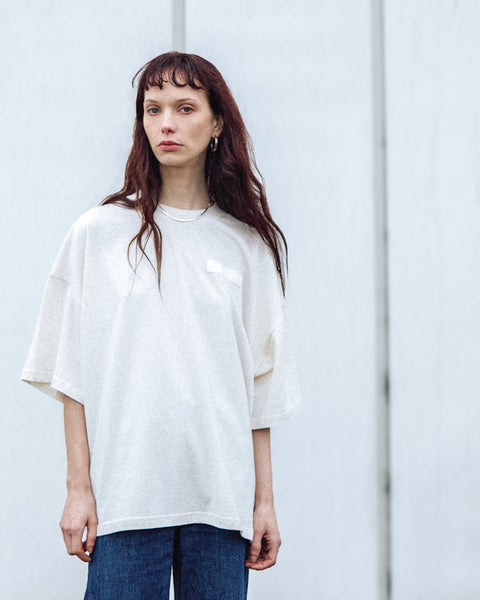 A female model is wearing the White Canvas Originals sustainable, oversized, genderless t-shirt, one size. The organic cotton natural color t-shirt has minimal modern aesthetics design allowing comfort and bringing self-confidence. This limited edition collection is made in Portugal to reduce environmental impact and guarantee high quality and durability of the products. There is a photo by the photographer Henrique Soares at the back of the t-shirt.