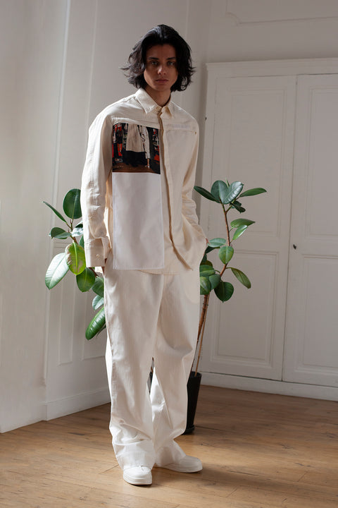Medhi is wearing the White Canvas essential shirt styled with the Trench Coat vertical panel made from deadstock cotton poplin. The panel has an exclusive print of a photo by the photographer Henrique Soares. Attach the panel to the essential pieces to personalize them and wear them your unique way. It is the perfect creative autumn accessory.