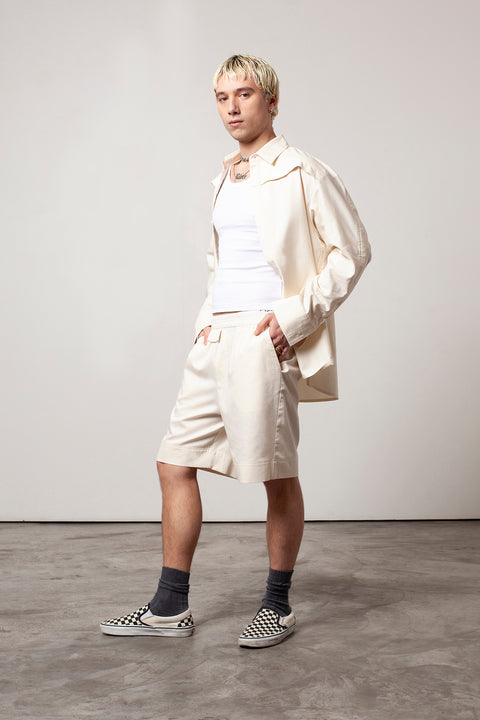 Clément is wearing White Canvas sustainable natural beige color, organic cotton, genderless, inclusive, casual short, size M styled with the essential shirt and white tank top. The Essential short has minimal modern aesthetics design allowing comfort and bringing self-confidence. A limited-edition production is made locally in France to reduce environmental impact and guarantee high quality and durability of the products. 