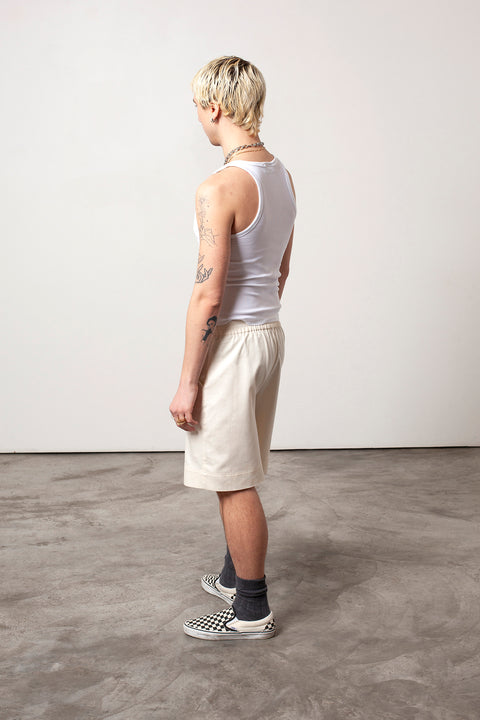 Clément is wearing White Canvas sustainable natural beige color, organic cotton, genderless, inclusive, casual short, size M styled with a white tank top. The Essential short has minimal modern aesthetics design allowing comfort and bringing self-confidence. A limited-edition production is made locally in France to reduce environmental impact and guarantee high quality and durability of the products. 