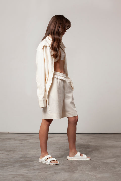 Léa is wearing White Canvas sustainable natural beige color, organic cotton, genderless, inclusive, casual short, size S styled with the essential shirt and natural jersey crop top. The Essential short has minimal modern aesthetics design allowing comfort and bringing self-confidence. A limited-edition production is made locally in France to reduce environmental impact and guarantee high quality and durability of the products. 