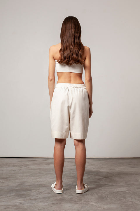Léa is wearing White Canvas sustainable natural beige color, organic cotton, genderless, inclusive, casual short, size S styled with a natural jersey crop top. The Essential short has minimal modern aesthetics design allowing comfort and bringing self-confidence. A limited-edition production is made locally in France to reduce environmental impact and guarantee high quality and durability of the products. 