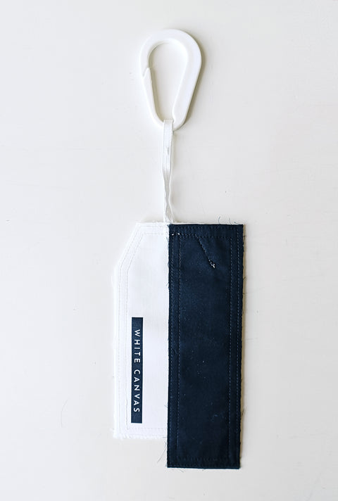 The White Canvas limited edition tag made in white and black cotton poplin leftover deadstock fabrics and with black artisanal eco-friendly screen print done locally in Paris in collaboration with RoStudio. Attach the panel to the essential pieces to personalize them and wear them your unique way. The tag is sold with key holder in recycled plastic made in collaboration with Samji Atelier