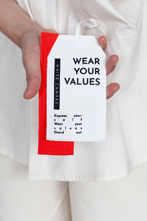 The White Canvas ESSENTIAL SHIRT with a limited edition tag made in white and red cotton poplin leftover deadstock fabrics and with black artisanal eco-friendly screen print done locally in Paris in collaboration with RoStudio. Attach the panel to the essential pieces to personalize them and wear them your unique way. The tag is sold with key holder in recycled plastic made in collaboration with Samji Atelier