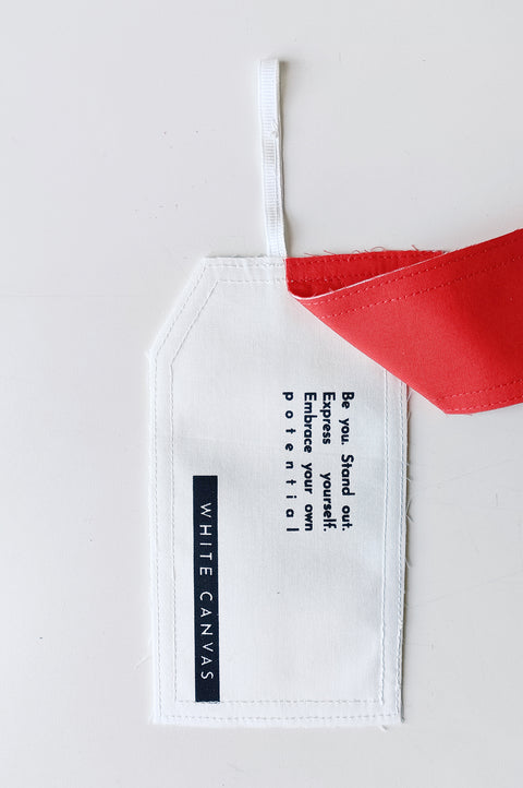 The White Canvas limited edition tag made in white and red cotton poplin leftover deadstock fabrics and with black artisanal eco-friendly screen print done locally in Paris in collaboration with RoStudio. Attach the panel to the essential pieces to personalize them and wear them your unique way. The tag is sold with key holder in recycled plastic made in collaboration with Samji Atelier