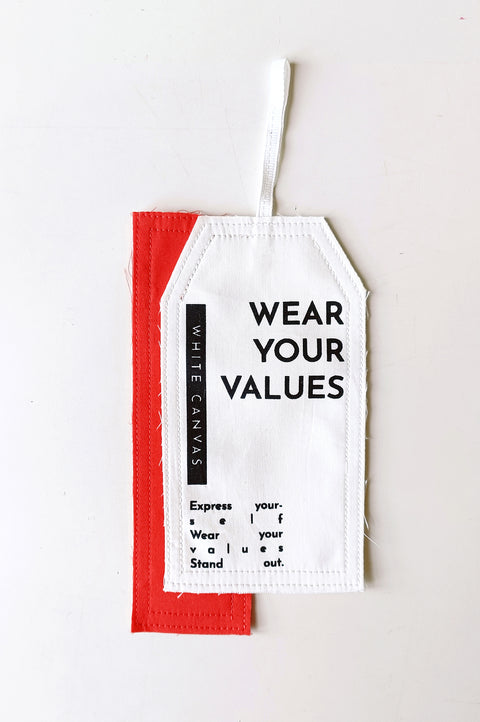 The White Canvas limited edition tag made in white and red cotton poplin leftover deadstock fabrics and with black artisanal eco-friendly screen print done locally in Paris in collaboration with RoStudio. Attach the panel to the essential pieces to personalize them and wear them your unique way. The tag is sold with key holder in recycled plastic made in collaboration with Samji Atelier