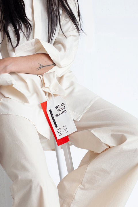 The White Canvas ESSENTIAL SHIRT with a limited edition tag made in white and red cotton poplin leftover deadstock fabrics and with black artisanal eco-friendly screen print done locally in Paris in collaboration with RoStudio. Attach the panel to the essential pieces to personalize them and wear them your unique way. The tag is sold with key holder in recycled plastic made in collaboration with Samji Atelier