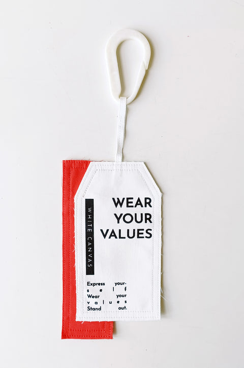 The White Canvas limited edition tag made in white and red cotton poplin leftover deadstock fabrics and with black artisanal eco-friendly screen print done locally in Paris in collaboration with RoStudio. Attach the panel to the essential pieces to personalize them and wear them your unique way. The tag is sold with key holder in recycled plastic made in collaboration with Samji Atelier