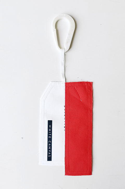 The White Canvas limited edition tag made in white and red cotton poplin leftover deadstock fabrics and with black artisanal eco-friendly screen print done locally in Paris in collaboration with RoStudio. Attach the panel to the essential pieces to personalize them and wear them your unique way. The tag is sold with key holder in recycled plastic made in collaboration with Samji Atelier