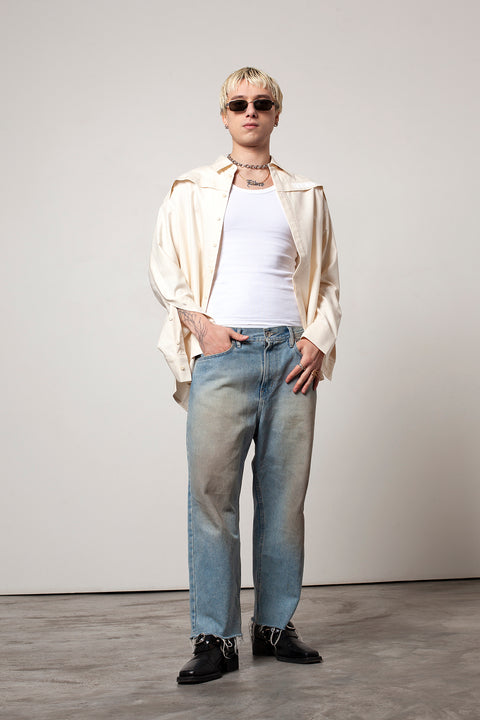 Clément is wearing White Canvas sustainable natural beige color, organic cotton oversized, genderless, inclusive, seasonless casual shirt, size L/XL styled with blue jeans and black sunglasses and shoes. The Essential shirt has minimal modern aesthetics design allowing comfort and bringing self-confidence. A limited-edition production is made locally in France to reduce environmental impact and guarantee high quality and durability of the products. 