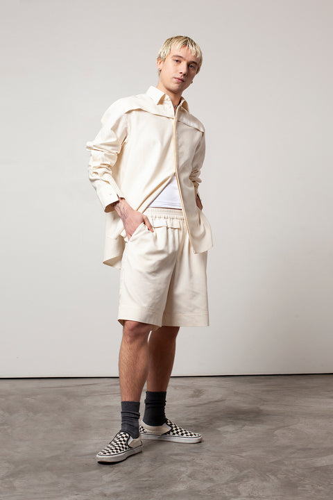 Clément is wearing White Canvas sustainable natural beige color, organic cotton, genderless, inclusive, casual short, size M styled with the essential shirt and white tank top. The Essential short has minimal modern aesthetics design allowing comfort and bringing self-confidence. A limited-edition production is made locally in France to reduce environmental impact and guarantee high quality and durability of the products. 